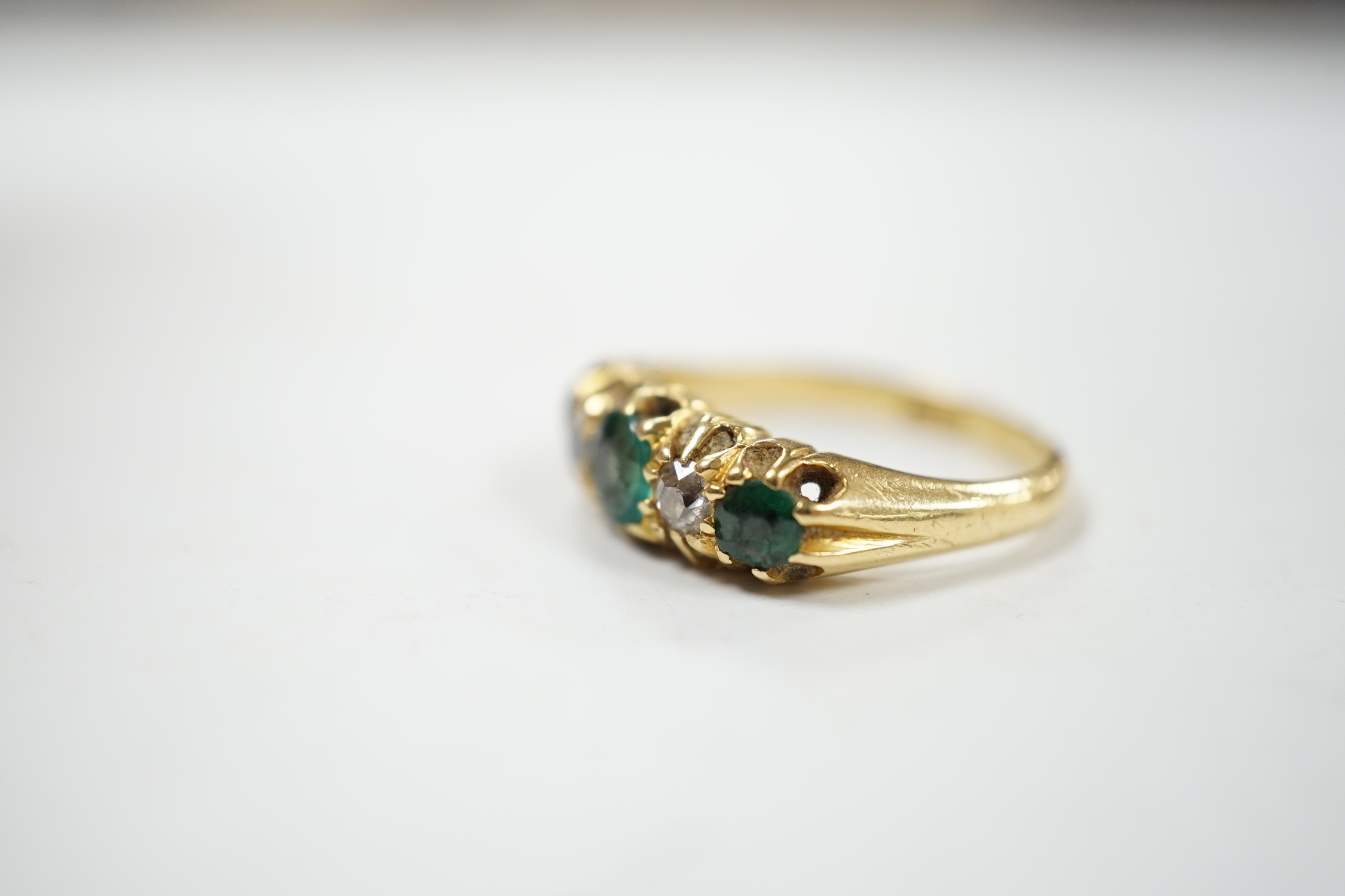 An early 20th century 18ct, three stone green garnet and two stone diamond claw set half hoop ring, size L, gross weight 4.8 grams.